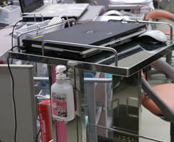 Trolley with laptop has a bottle of hand disinfectant attached to encourage hand hygiene.